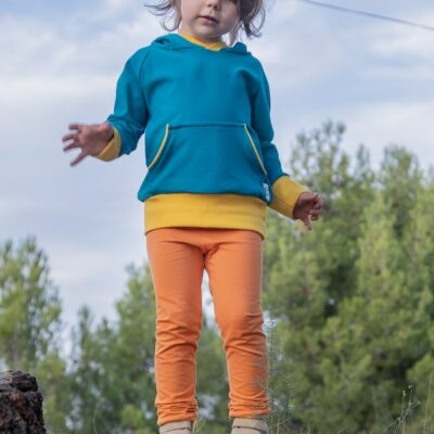 Mini dressed in Dirusario dino sweatshirt and orange Lisa leggings in front of a tree.