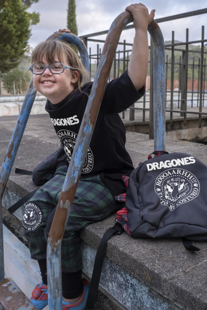 Modelo vestida con camiseta negra con diseño de Dragones, pantalón de cuadros verdes y mochila de Dragones. 